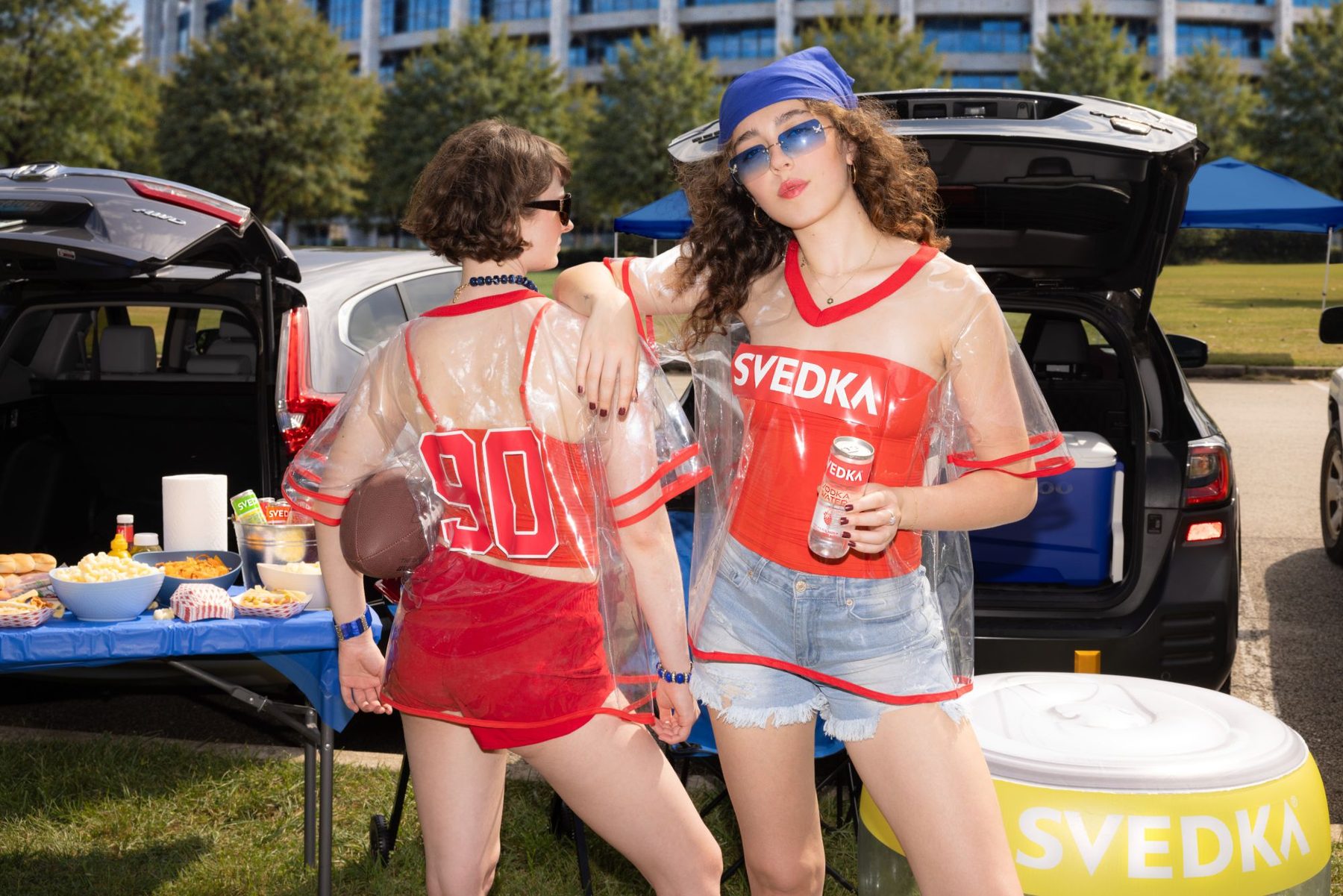 Two tailgaters in the clear Strawberry Oversized Jersey, one showing the #90 on the back, holding a football and a can of SVEDKA Vodka Water